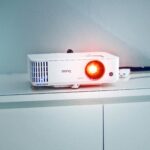 Stylish white projector on a cabinet with glowing lens, perfect for presentations and media rooms.